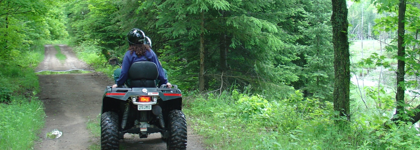 Two people riding an ATV through a forested trail.