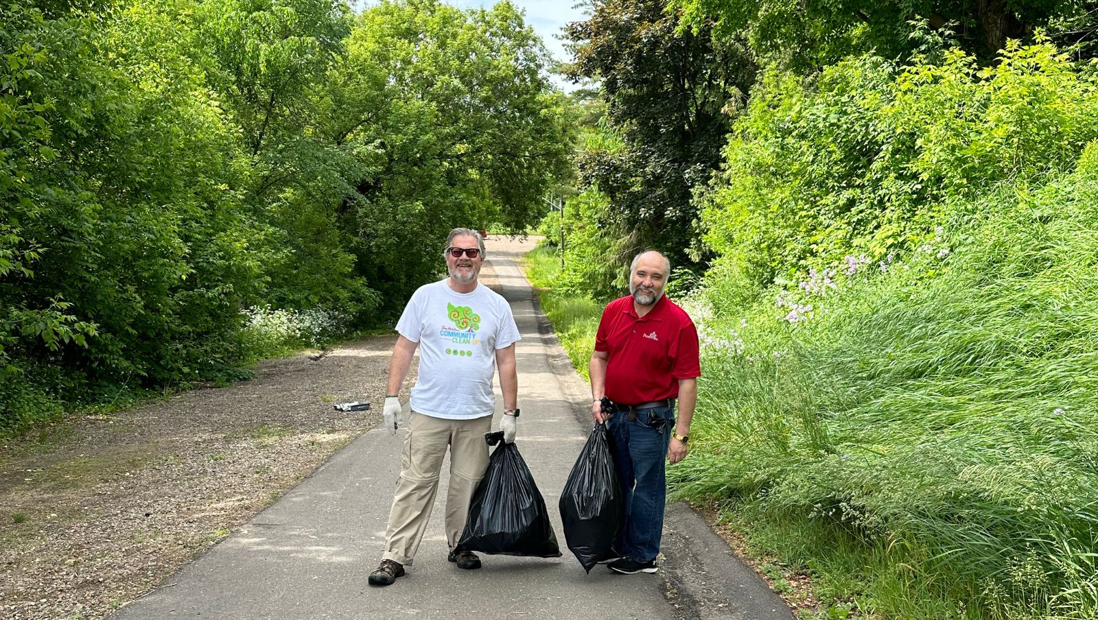 Two men with garbage bags on an outdoor path.
