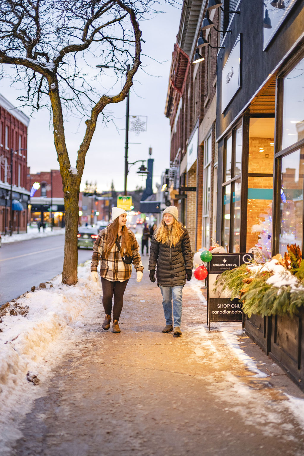 Two women walking down a snowy, commercial street.