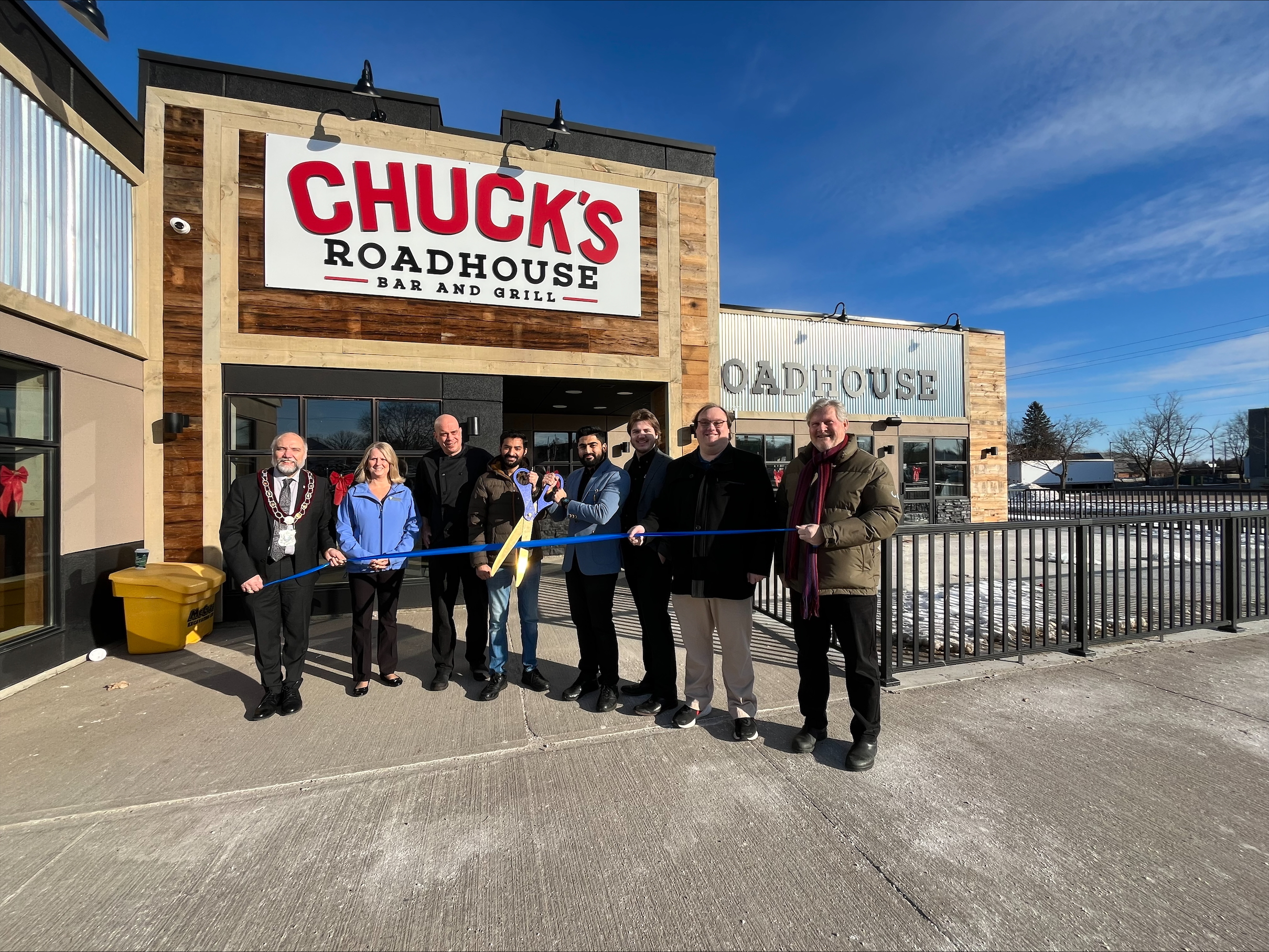 A group of people with giant scissors and ribbon for a celebration. 