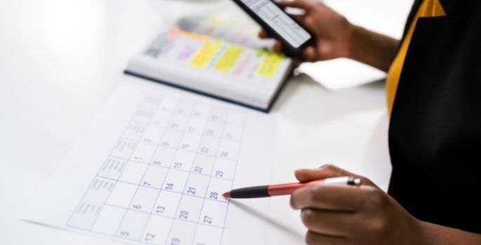 A photo of a person looking over a calendar with a phone in hand.